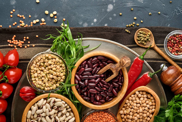 Legumes, lentils, chickpea, beans assortment, tasty appetizing ingredients spices grocery for cooking healthy kitchen on black table. Weight loss diet and fight against cholesterol concept. Top view. - Photo, image