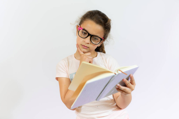 Милая маленькая девочка стоит и читает книгу на белом фоне - Фото, изображение