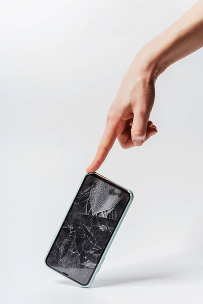 白い背景に女性の手に壊れた画面を持つスマートフォン。スマートフォン用のクラッシュ保護強化ガラス。壊れた画面を持つ高価なスマートフォン - 写真・画像