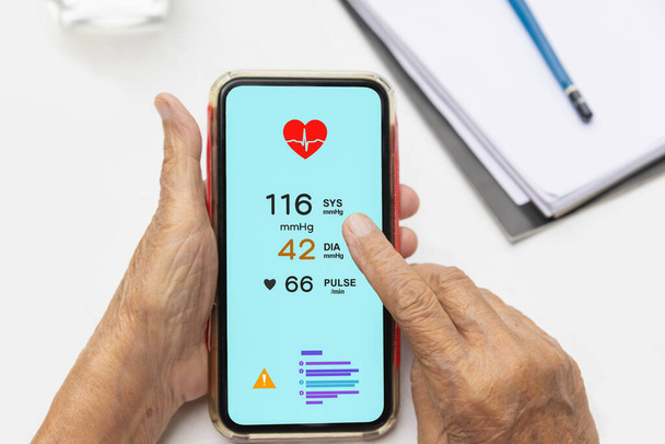 Senior mulher verificando a pressão arterial (hipertensão) vai telefone celular - Foto, Imagem