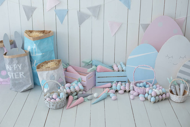 Colorful Easter room interior. Baskets with lot colorful Easter eggs and carrots! Spring home decoration and easter decor. Holiday flags on wooden white wall. Children's room in the Easter style - Valokuva, kuva