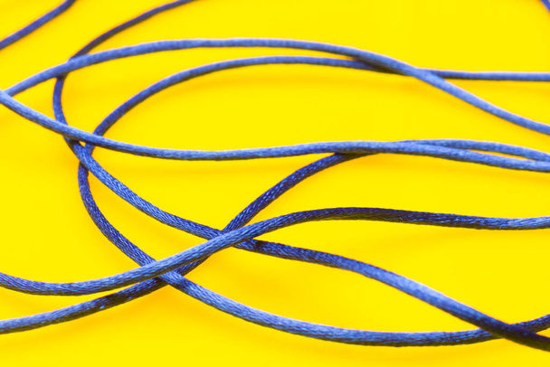 Dunne blauwe koord op gele achtergrond, rommelige draad van de spoel zonder volgorde, mengeling van koord. - Foto, afbeelding