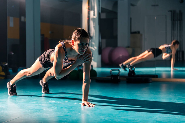Um exercício feminino jovem no ginásio e fazendo um exercício de torneiras de ombro. - Foto, Imagem