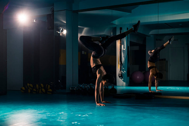 Une jeune femme en forme faisant un stand de main classique et des variations d'exercices de gymnastique dans la salle de gym - Photo, image