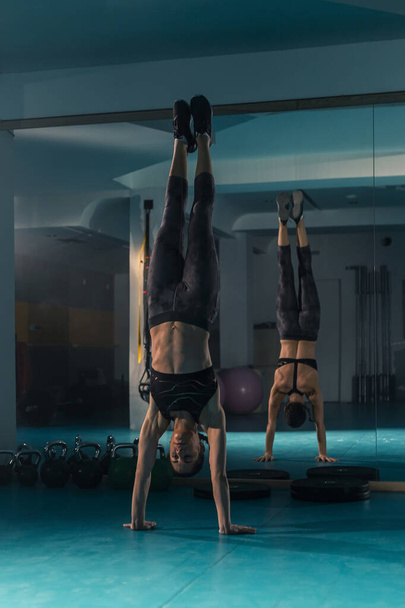 A young and fit female doing a classical hand stand and variations of gymnastics exercises in the gym - Photo, Image