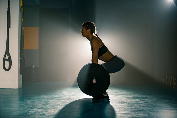 Eine fitte junge Frau, die von der Seite fotografiert wird, beim Kreuzheben im Fitnessstudio. - Foto, Bild