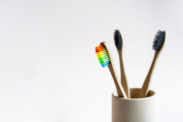 Bamboe tandenborstels in een houten glas op een licht roze achtergrond. Minimalistische stilleven van eco-vriendelijke badkamerproducten. Geen afval, geen plastic, duurzaam lifestyle concept. - Foto, afbeelding
