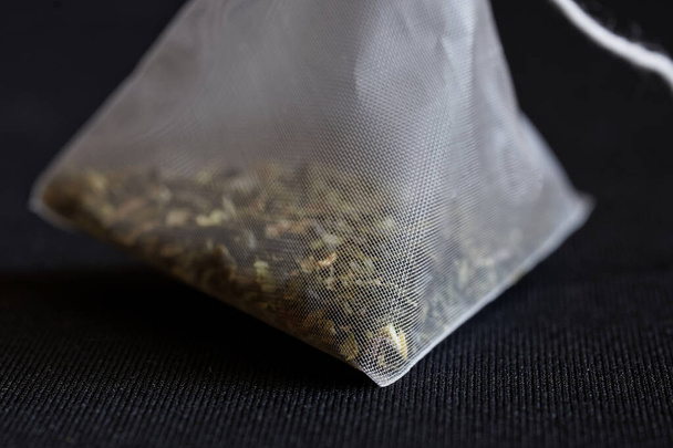 Biała piramida torebka herbaty z zielonej herbaty leży na czarnym tle teksturowane. Makro. Mroczny styl. Zbliżenie. Skupienie selektywne - Zdjęcie, obraz