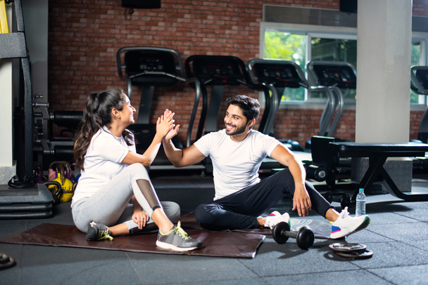 Indian young couple in gym resting or taking break from exercise, drinking water, showing positive expressions - Photo, Image