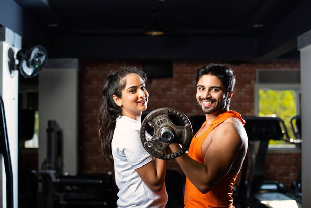 Ινδικό Ασιατικό Νεαρό ζευγάρι γυμνάζεται στο γυμναστήριο. Ελκυστική γυναίκα και όμορφος άντρας σε φόρμα προπονούνται στο σύγχρονο γυμναστήριο - έννοια της υγείας και της φυσικής κατάστασης - Φωτογραφία, εικόνα