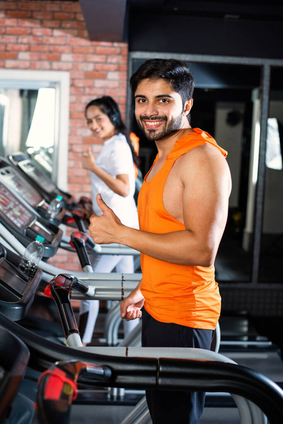 Indian asian attractive couple doing cardio training program in fitness center or gym, selective focys - health and fitness concept - Photo, Image