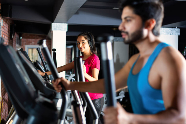 Indian asian attractive couple doing cardio training program in fitness center or gym, selective focys - health and fitness concept - Photo, Image