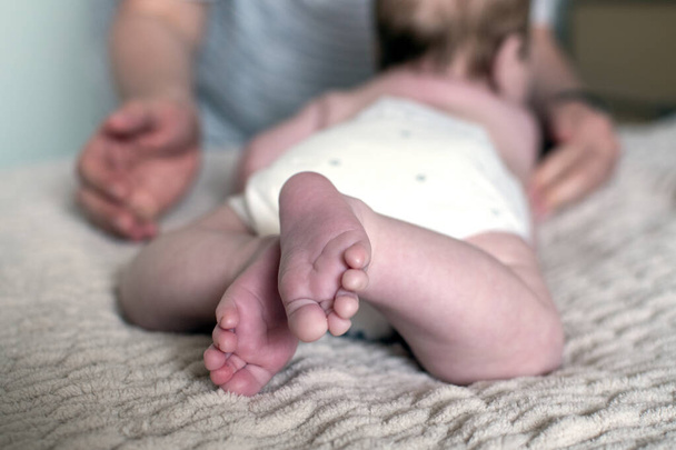 Gros plan d'un bébé pieds. Enfant de 3 mois couché sur le lit. Les mains de maman au premier plan. Concept de garde d'enfants. Concentration sélective - Photo, image