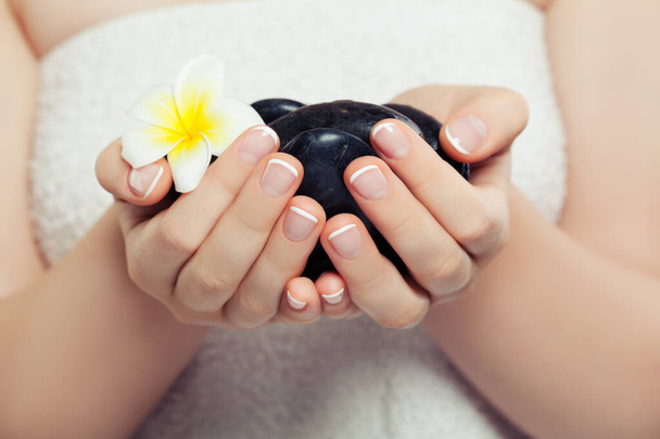 Concept de spa avec pierres de massage noires et fleur tropicale dans de belles mains de femme - Photo, image
