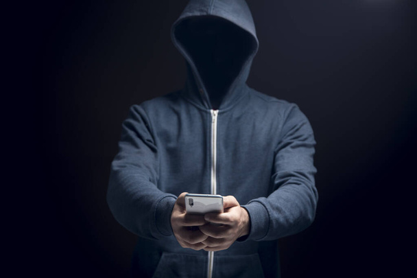 holds the phone on a dark background. hacker concept - Foto, afbeelding