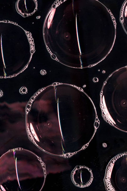 Seifenblasen schäumen auf Glasoberfläche isoliert auf schwarzem Hintergrund. Licht in der dunklen Nacht. Abstrakte Lichtdekoration. Nachtclub abstrakte Tapete - Foto, Bild