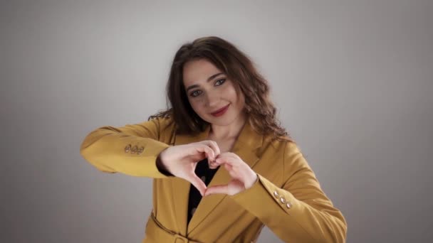 Portrait of young caucasian woman showing heart shape by her hands on white background in slowmo - Filmati, video