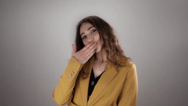 Młoda kobieta w żółtej kurtce z długimi kręconymi włosami wysyła pocałunek powietrza w spowolnieniu na białym tle - Materiał filmowy, wideo