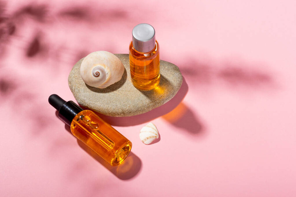 Tanning oil. Cosmetic products next to seashells in sunbeams on a pink background. Sun protective cosmetics. - Фото, изображение