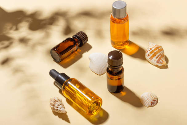 Tanning oil. A set of cosmetics next to seashells in the sunbeams on a pink background. Cosmetics for sun protection. - Photo, image