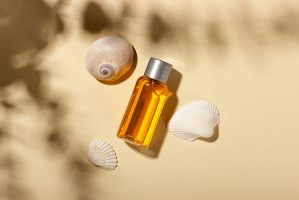 Tanning oil. Cosmetic products next to seashells in sunbeams on a pink background. Sun protective cosmetics. - Fotó, kép