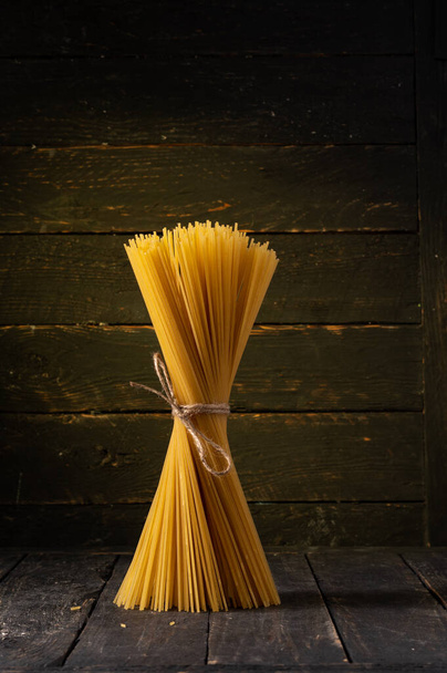 Spaghetti tied with craft rope. Spaghetti on a wooden background. Vertical frame. - Foto, afbeelding