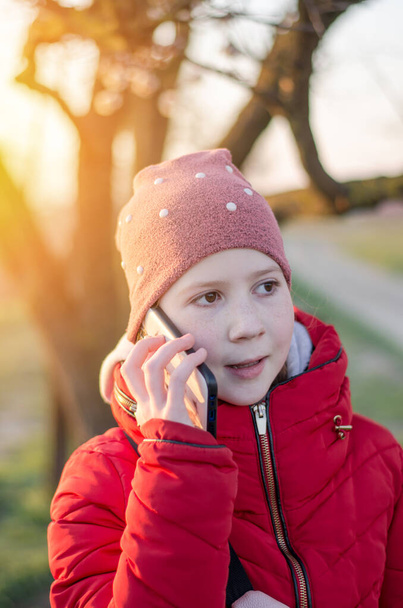Desetiletá holka mluví na mobilním telefonu v přírodě. Dívka cestovatel v paprscích večerního slunce. - Fotografie, Obrázek