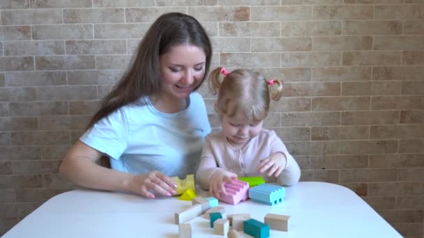 Милая маленькая девочка и молодая женщина сидят на кухне и играют со строительными блоками - Кадры, видео