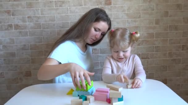 Linda niña y mujer joven sentada en la cocina y jugando con bloques de construcción - Metraje, vídeo