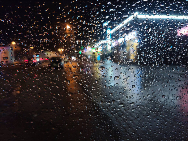 Краплі на вікні автомобіля в нічному місті на тлі яскравих знаків магазинів і проїжджих автомобілів
 - Фото, зображення