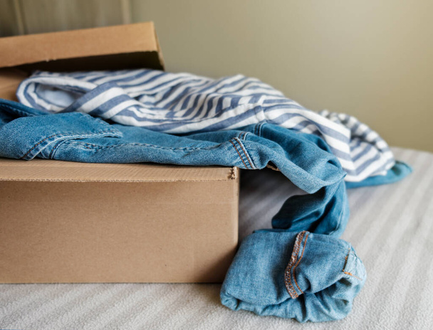 Cardboard box with pre owned clothes inside. Sustainable fashion, resale used clothes - Foto, Imagem