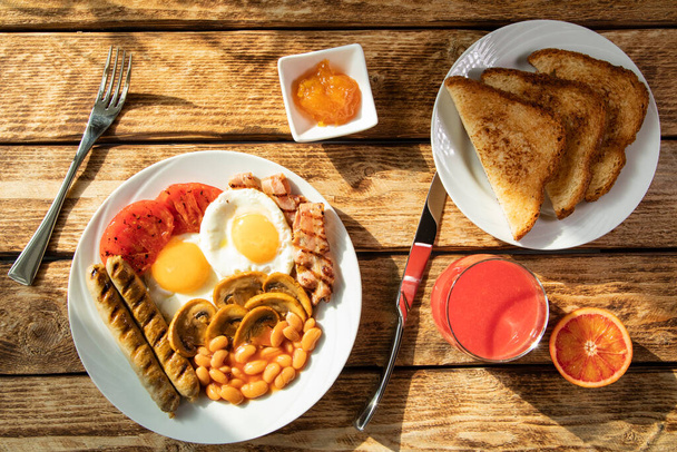 Традиційний ранок Англійський сніданок - яєчний сніданок, білі боби, помідори, гриби, сосиски і варення абрикоса з класичною Англією смажені тости на білій тарілці і червоному апельсиновому соку зверху. - Фото, зображення