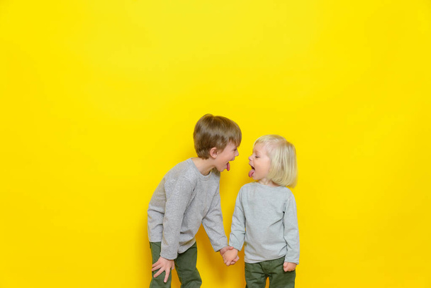 Two beautiful boys show each other tongues and have fun on a yellow background - Fotografie, Obrázek