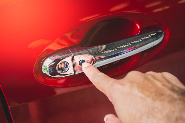 La main humaine appuyait sur le bouton d'entrée sans clé sur la poignée de porte de la voiture rouge - Photo, image