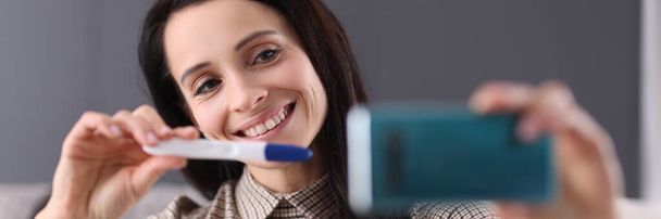 Uśmiechnięta kobieta pokazuje test ciążowy w smartfonie - Zdjęcie, obraz