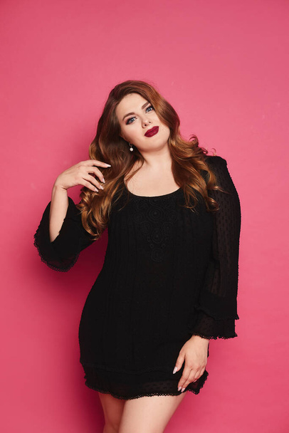 Young plus size model woman with full red lips and wavy hair posing over pink background. Vertical isolated studio shoot - Φωτογραφία, εικόνα