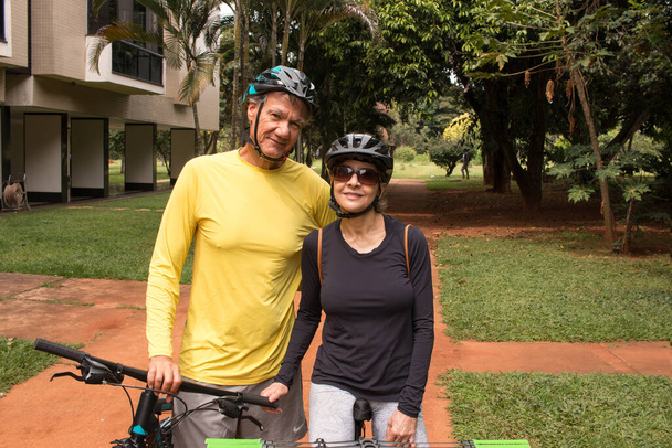 Volwassen echtpaar buiten in een stedelijk gebied op hun fietsen - Foto, afbeelding