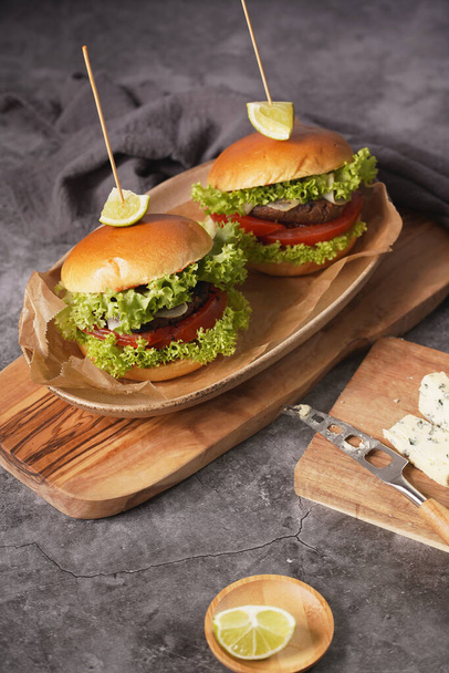 Two hamburgers with vegetarian patty, lettuce, tomatoes and a slice of lime on wooden board - Foto, imagen