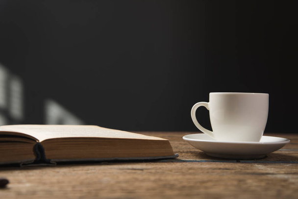 boek en een kop koffie op een houten tafel - Foto, afbeelding