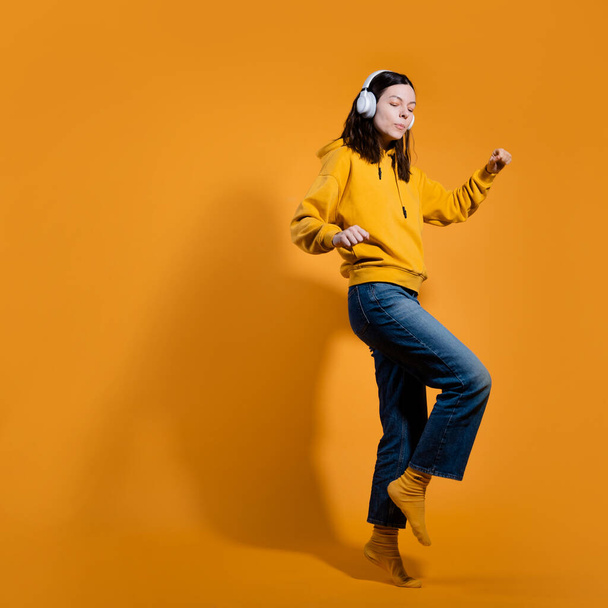Happy dancing music lover. A young woman in a yellow hoodie with white wireless headphones, - Photo, image