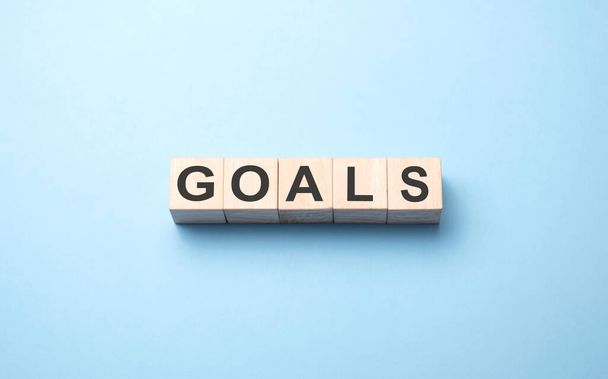 Goals word written on wood block. Goals word is made of wooden building blocks lying on the blue table. Business concept, yellow background - Foto, afbeelding