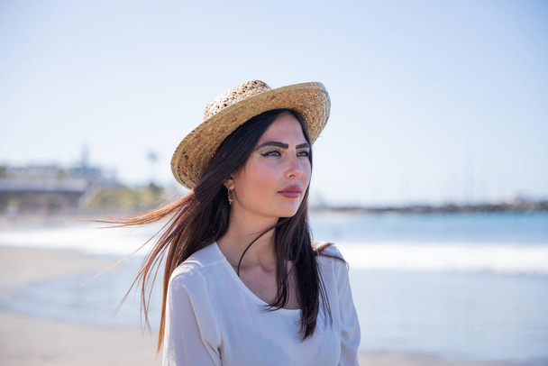 Portré egy vonzó és magabiztos kaukázusi lányról a parton. Lazít és nyári kalapot visel. - Fotó, kép