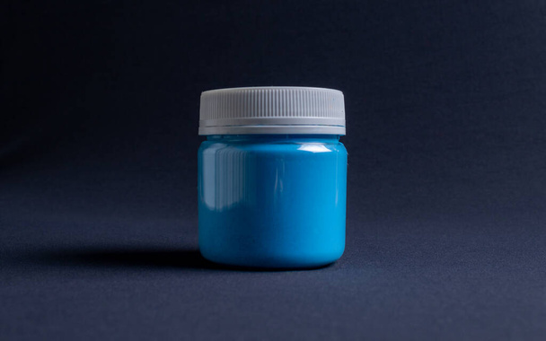 A jar containing blue glitter resin on a dark black background. Used for various purposes in industry and at home in the adaptation of furniture and objects for interior decoration. - Photo, Image