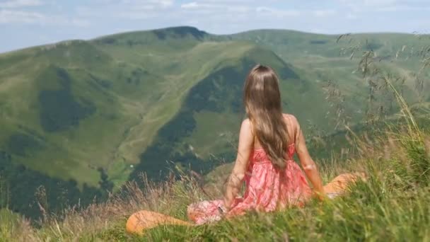 Junge Frau mit langen Beinen legt sich auf eine grüne Wiese und ruht sich an einem sonnigen Tag in den sommerlichen Bergen aus und genießt die Aussicht auf die Natur. - Filmmaterial, Video