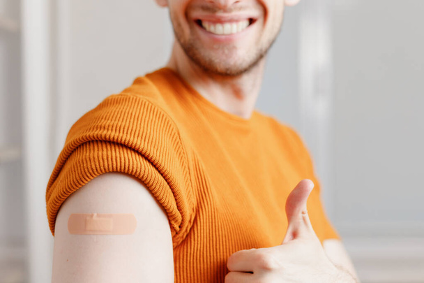 Homme avec bandage adhésif plâtre sur l'épaule montrant le pouce geste après l'injection vaccin. - Photo, image
