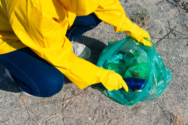 Γυναίκα με αδιάβροχο μαζεύει σκουπίδια στο πάρκο. - Φωτογραφία, εικόνα