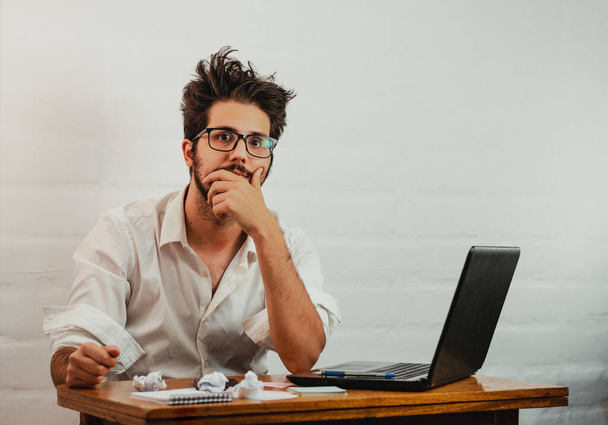 Latin man in the office, gesturing fatigue and stress. Looking straight ahead bored and disheveled. Work at home concept. Copy space. - 写真・画像
