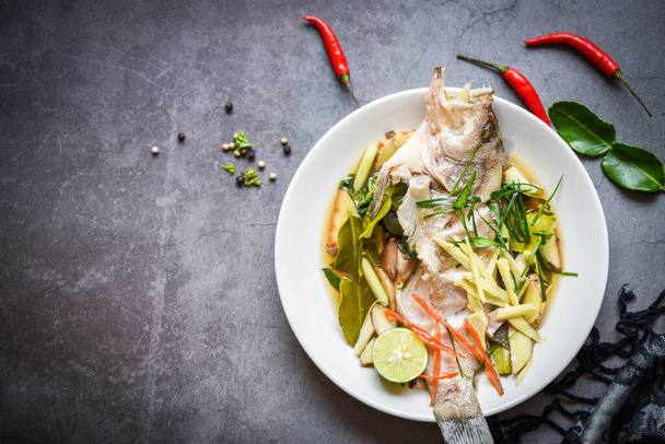 Gestoomde vis op wit bord met gember chili kruiden en specerijen citroenlimoen op donkere achtergrond, gestoomde tandbaars vis met sojasaus chinees eten stijl - Foto, afbeelding