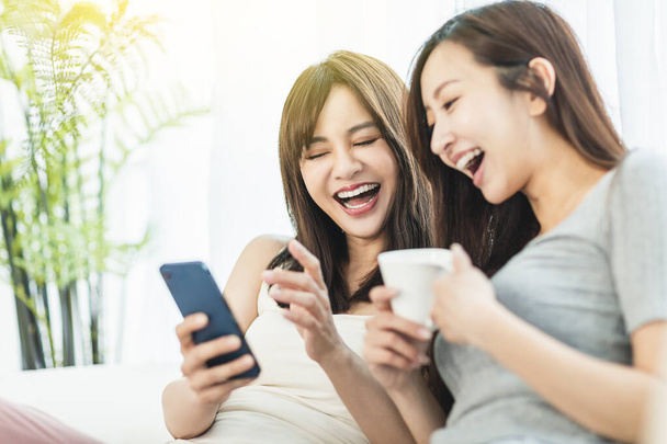 幸せな若いです女性見ます彼らのスマートフォン座っています上のソファに家 - 写真・画像