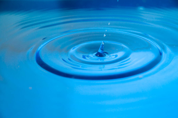 A kék vízcseppek elérik a víz felszínét. - Fotó, kép